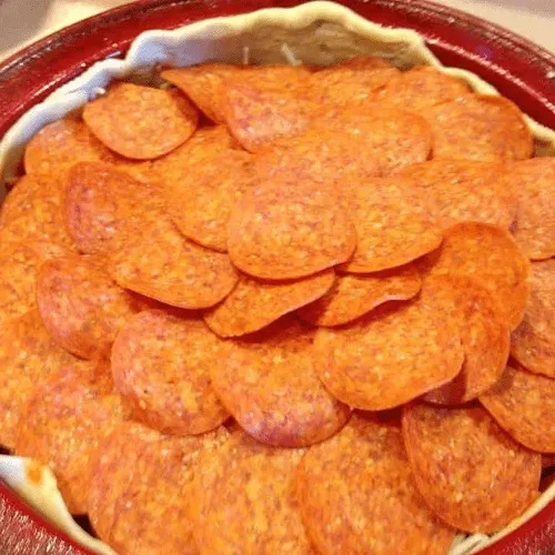 Deep dish pan filled with a generous layer of pepperoni slices, assembling a copycat Pizza Hut Priazzo deep-dish pizza.