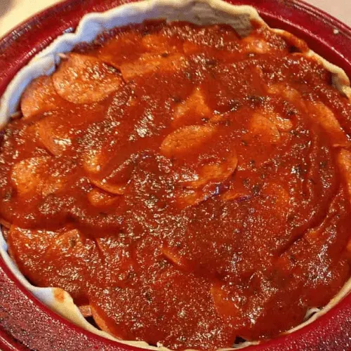 Deep dish pan filled with pepperoni slices covered with a layer of pizza sauce, assembling a copycat Pizza Hut Priazzo deep-dish pizza.