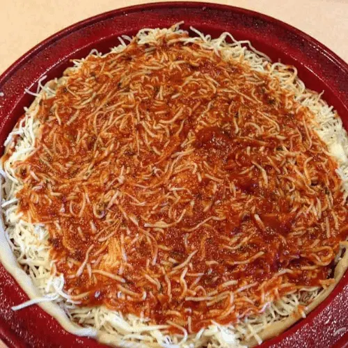 Deep dish pan filled with shredded mozzarella cheese covered with a layer of pizza sauce, completing the assembly of a copycat Pizza Hut Priazzo deep-dish pizza.