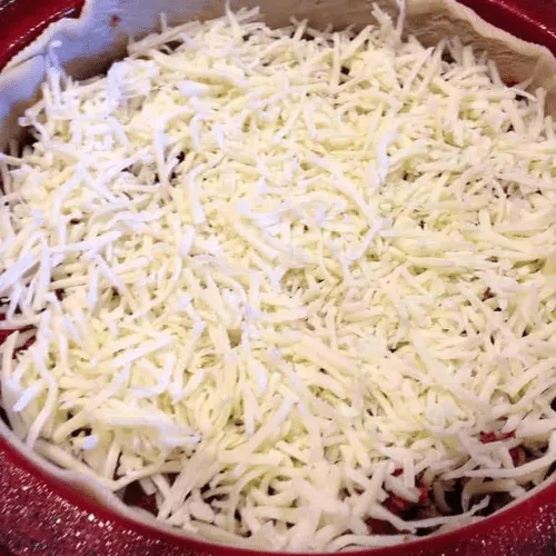 Deep dish pan filled with a layer of shredded mozzarella cheese, assembling a copycat Pizza Hut Priazzo deep-dish pizza.