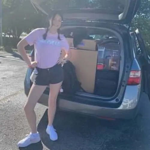 van loaded with dorm essentials and college student standing near.