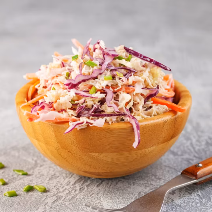 A vibrant bowl of creamy coleslaw with a tangy twist, featuring green and purple cabbage, and shredded carrots, perfect for summer gatherings.