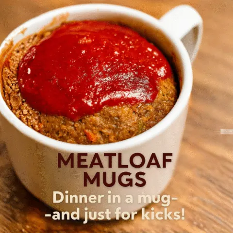 Close-up of a meatloaf mug filled to the brim with golden-brown meatloaf topped with glossy ketchup, served in a white ceramic mug on a wooden surface&mdash;perfect for cozy, microwave-friendly dinners.