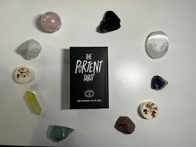 A photo featuring various crystals and The Portent Tarot card deck arranged neatly on a white table.