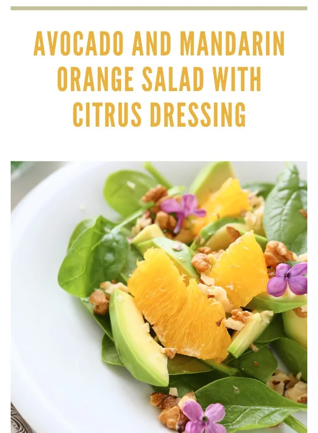 Plate of avocado and mandarin orange salad with spinach, almonds, and citrus dressing garnished with edible flowers.