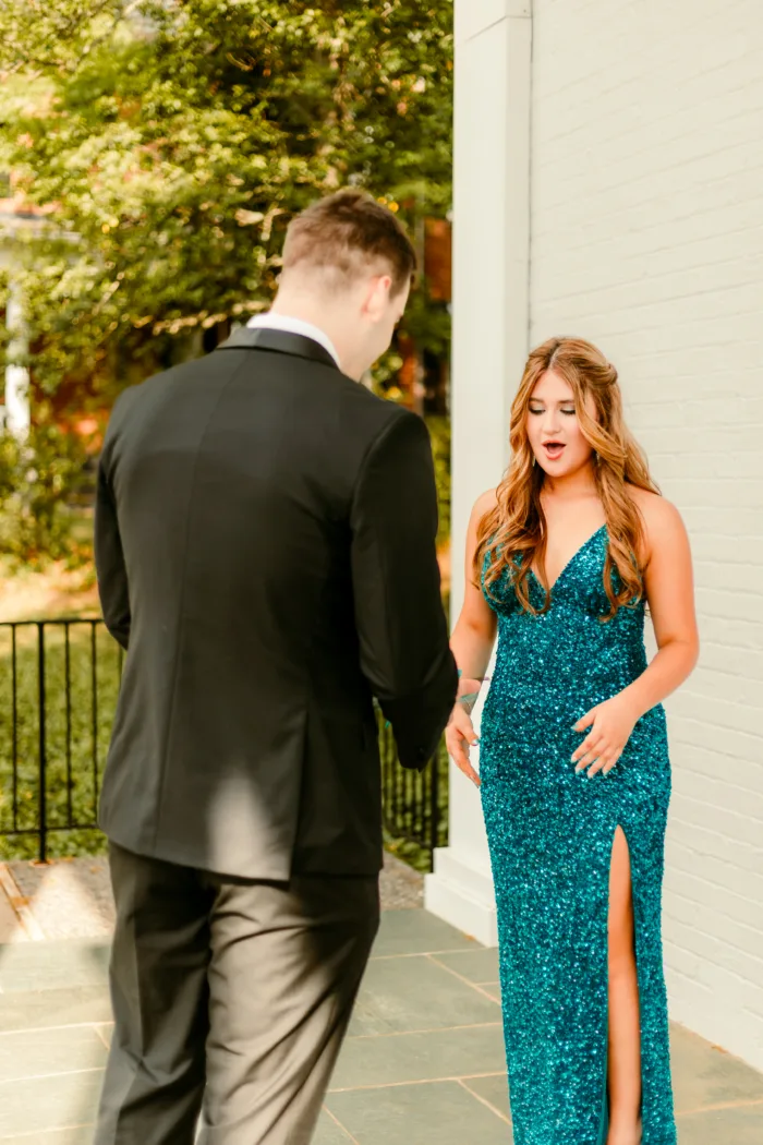 Young woman in a teal sequin dress reacts excitedly to a young man in a black tuxedo presenting a teal corsage during Prom 2024.