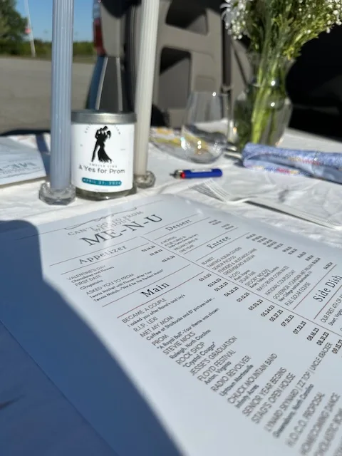 Close-up of a 'Me-n-U' prom proposal setup on a romantic table, featuring a detailed menu and a themed wine bottle, ready for the big question.