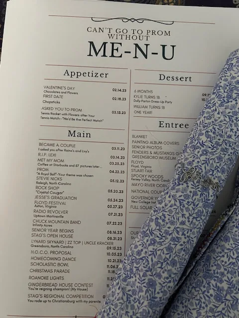 An inventive promposal menu displayed next to a blue floral napkin, showcasing a timeline of relationship milestones formatted as a dining menu.