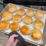 A dozen golden homemade hamburger buns cooling on a baking tray fresh out of the oven.