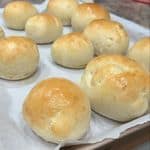 A batch of golden homemade hamburger buns cooling on a baking sheet, fresh out of the oven.