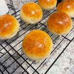 Six freshly baked golden homemade hamburger buns cooling on a wire rack.