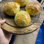 Four golden homemade hamburger buns topped with sesame seeds on a wooden plate, fresh from the oven.