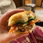 A close-up of a hand holding a homemade hamburger with lettuce, tomato, and a homemade bun.