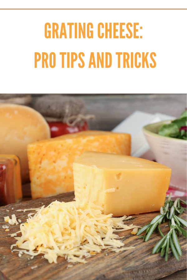 Block of cheddar cheese being freshly grated on a wooden board with a stainless steel grater.