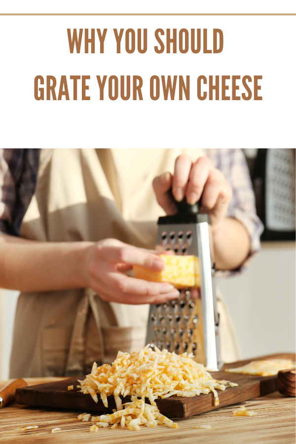 Block of cheddar cheese being freshly grated on a wooden board with a stainless steel grater.