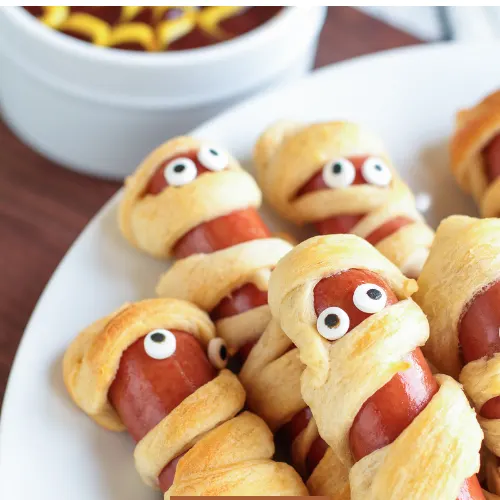 Spooky Halloween mummy dogs wrapped in crescent dough, topped with mustard eyes, perfect for kids and parties