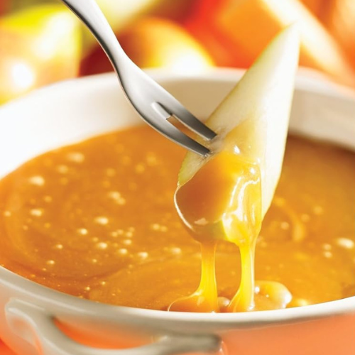 Close-up of a caramel fondue with a piece of fruit being dipped in rich, golden caramel sauce, ideal for dessert.