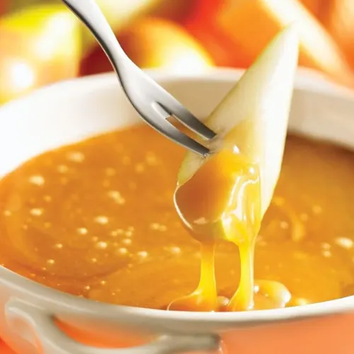 Close-up of a caramel fondue with a piece of fruit being dipped in rich, golden caramel sauce, ideal for dessert.