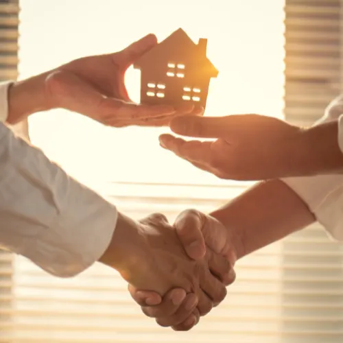 real estate deal with realtor and buyer shaking hands under a wooden house with light coming through window