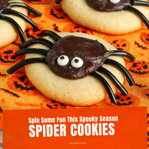 Close-up of Halloween Spider Cookies made from soft sugar cookies, black frosting, licorice legs, and candy eyes, styled on orange pumpkin-patterned fabric for a festive and spooky presentation.