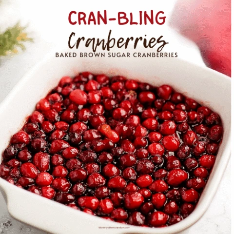 Close-up image of baked brown sugar cranberries in a white ceramic baking dish, styled with festive holiday props like pine sprigs and a red napkin. Cranberries are glossy, caramelized, and glistening under warm lighting &mdash; perfect for a cozy Thanksgiving or Christmas side dish.