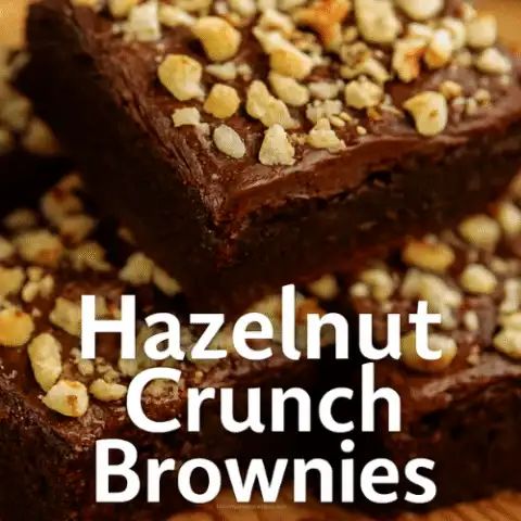 Stacked Hazelnut Crunch Brownies with glossy chocolate frosting and chopped hazelnuts on top, styled on a rustic surface with warm lighting and cozy holiday props.