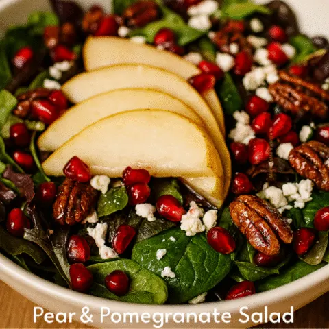 Overhead shot of a vibrant pear and pomegranate salad in a white bowl, featuring sliced pears, pomegranate seeds, candied pecans, crumbled feta, and mixed greens. Text overlay reads &ldquo;A PEAR-FECT SALAD!&rdquo; with &ldquo;Pear & Pomegranate Salad&rdquo; as subtitle. Styled with warm lighting and shallow depth of field for a festive, high-quality Pinterest image.