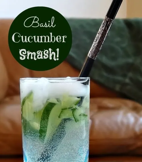 A refreshing basil cucumber smash cocktail in a tall glass, garnished with cucumber slices and ice, served with an elegant straw on a cozy background.