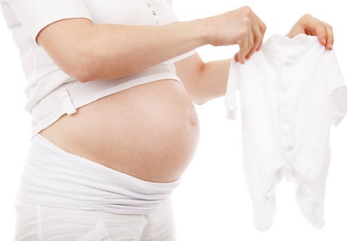 pregnant woman with belly showing holding white onesie preparing for the perfect delivery day
