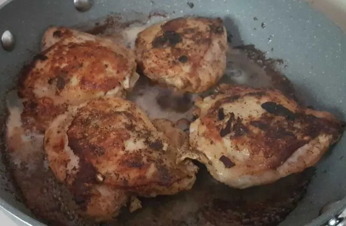 Chicken thighs being browned in a skillet, a step in preparing Instant Pot Arroz con Pollo