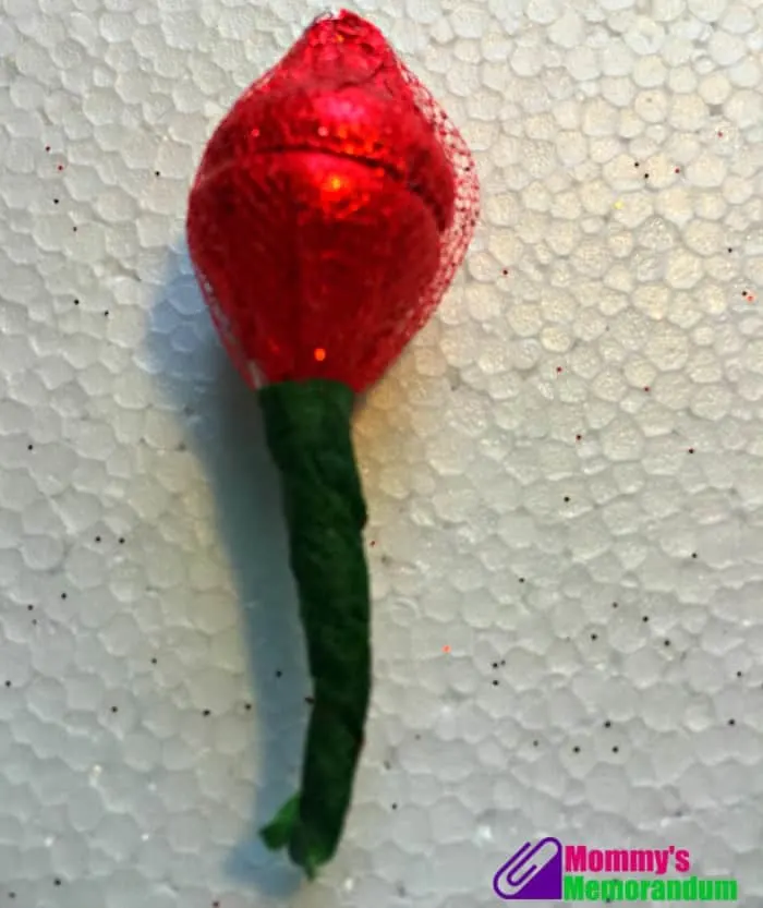 Finished Hershey Kisses rosebud wrapped in red tulle with green floral tape for a DIY project.