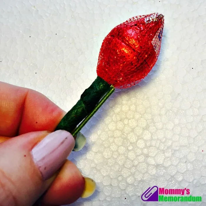 Hand holding a Hershey's Kiss rose wrapped in red foil with a green stem