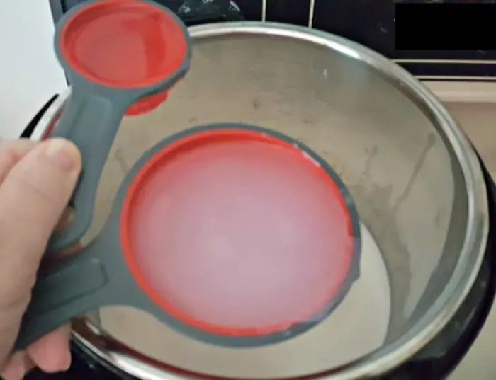 A close-up photo of a hand pouring water into a bowl containing milk, sugar, and salt for Instant Pot rice pudding.