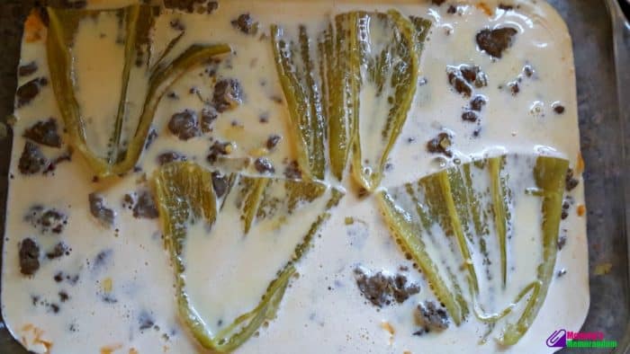 Egg mixture being poured over sausage, chiles, and cheese layers in a baking pan for green chile quiche.