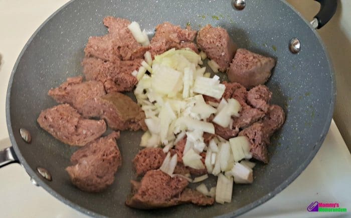 Jennie-O turkey sausage browning in a pan with chopped onions, ready for a savory green chile quiche.