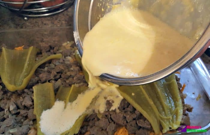 Egg mixture being poured over sausage, chiles, and cheese layers in a baking pan for green chile quiche.