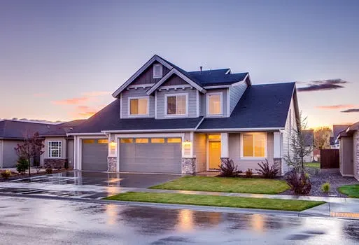 beautiful home with curb appeal lights on at twilight and ground wet from rain