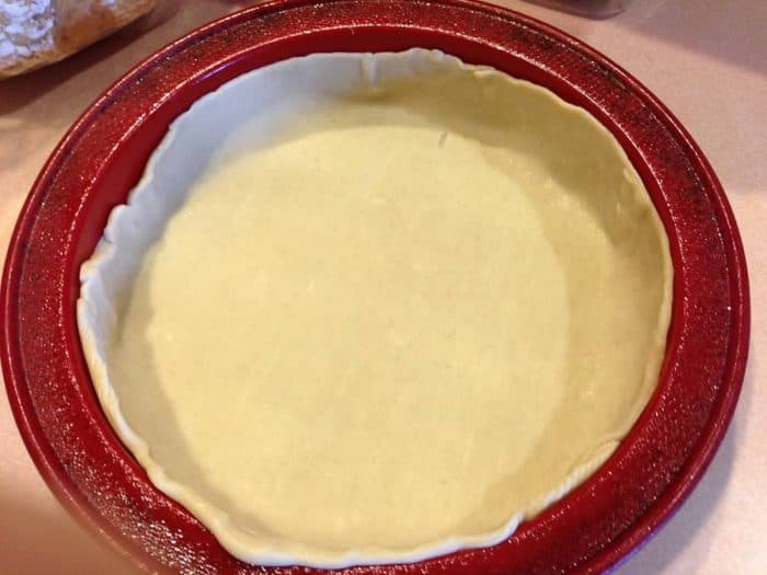 Pie crust placed in a deep red pan, ready for making a copycat Pizza Hut Priazzo deep-dish pizza.