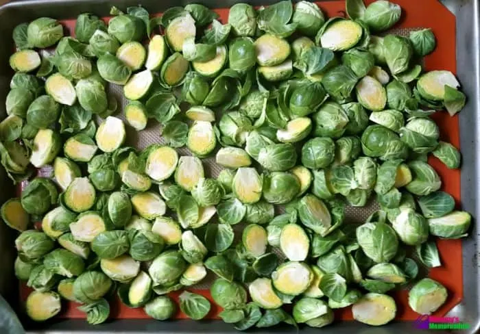 Buttered Brussels sprouts spread in a single layer on a baking sheet, ready for roasting