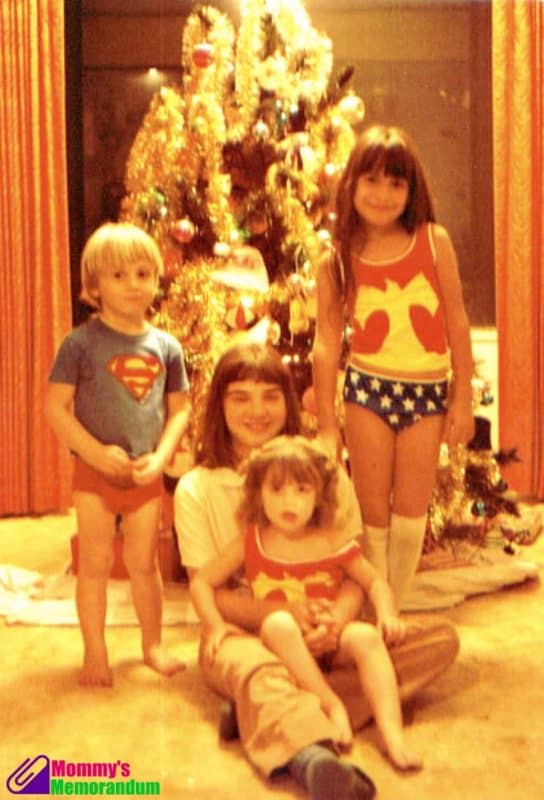 Four children in superhero-themed pajamas posing in front of a Christmas tree in the 1970s